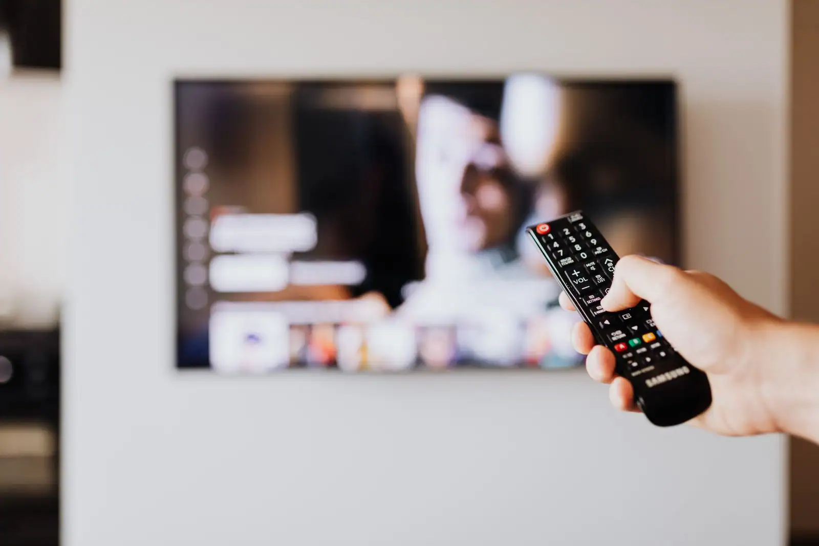 Personne tenant une télécommande devant un téléviseur affichant une application de streaming vidéo