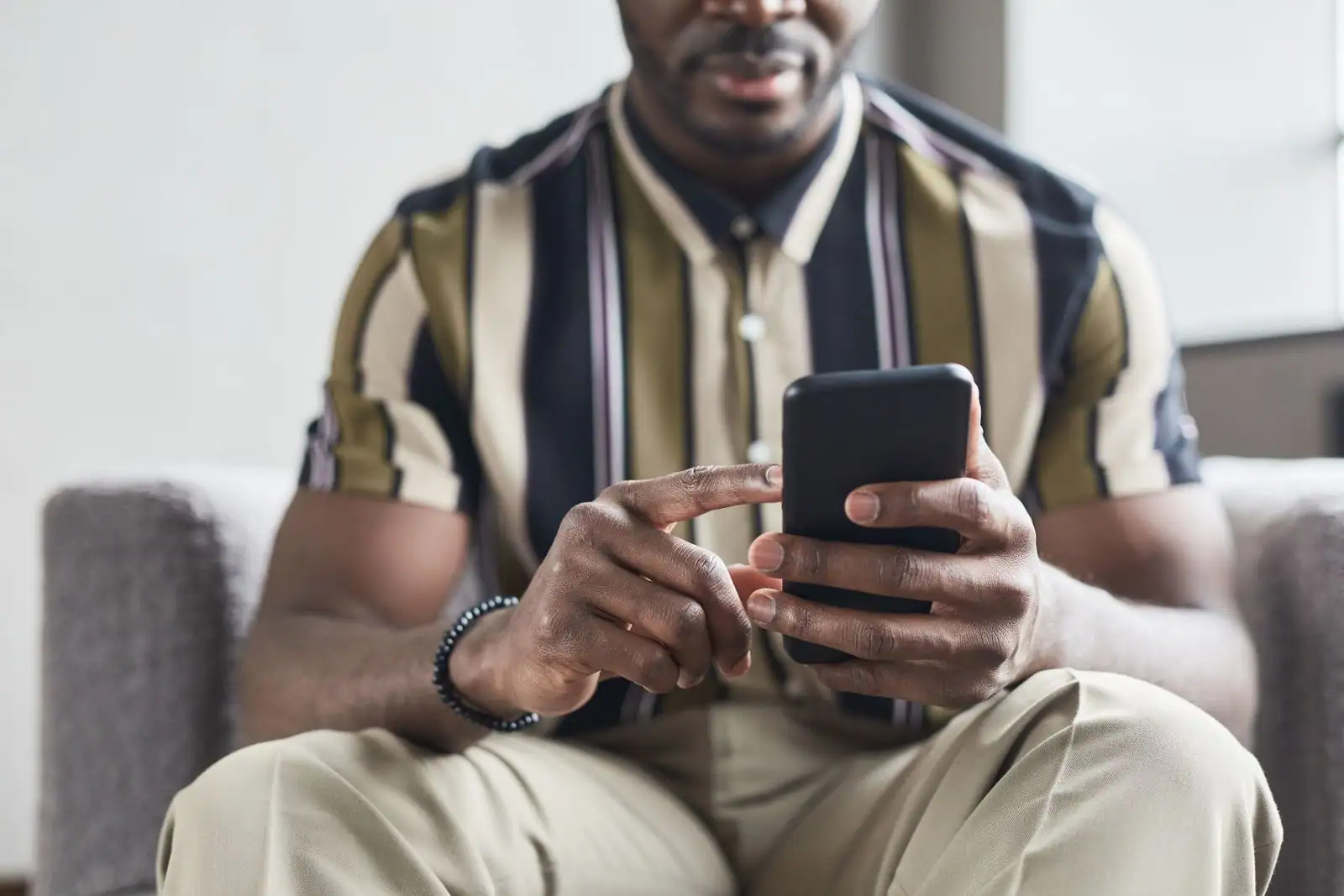 Homme assis sur un canapé utilisant une application sur son smartphone, touchant l'écran