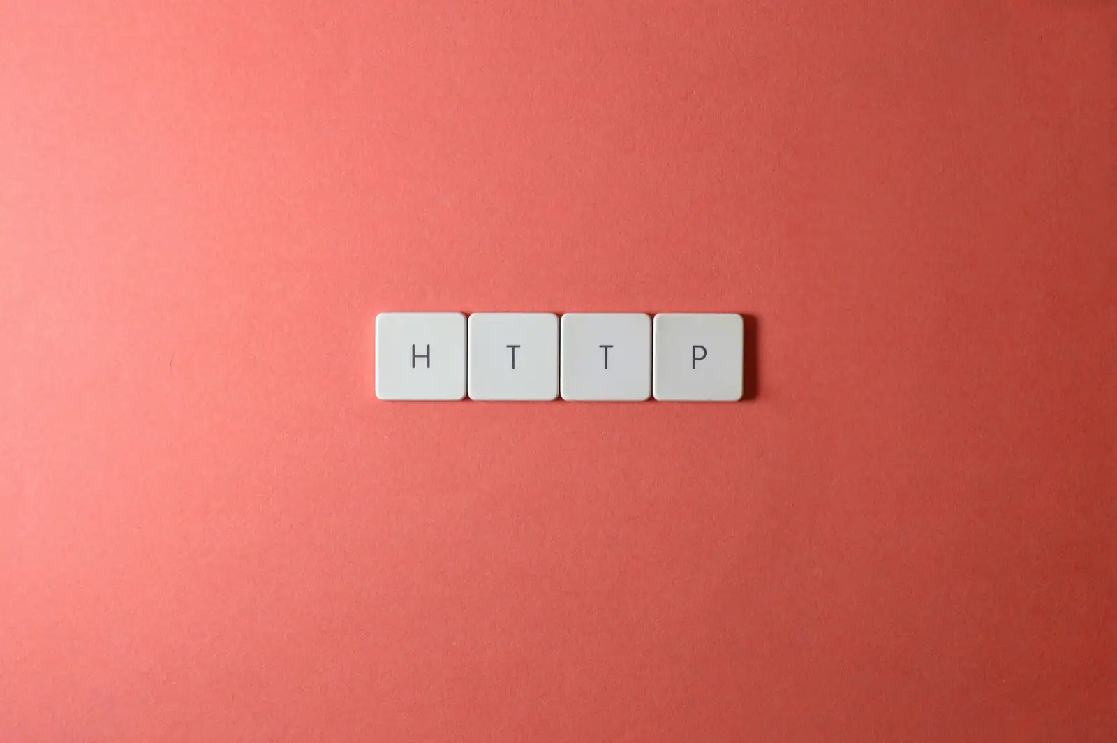 Quatre touches de clavier blanches formant le mot HTTP, disposées sur un fond corail uni