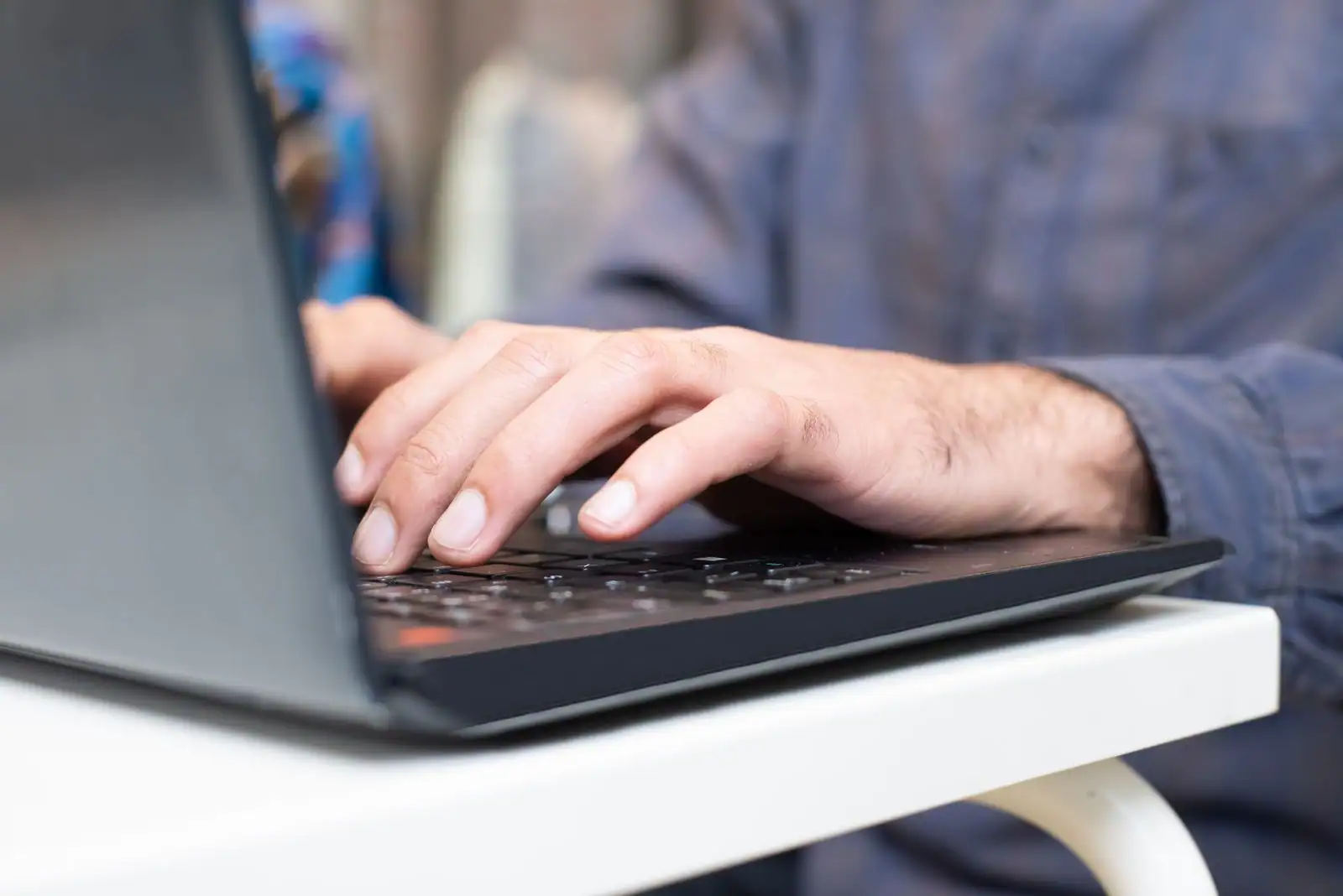 Une personne tape sur le clavier d'un ordinateur portable, posé sur un bureau.