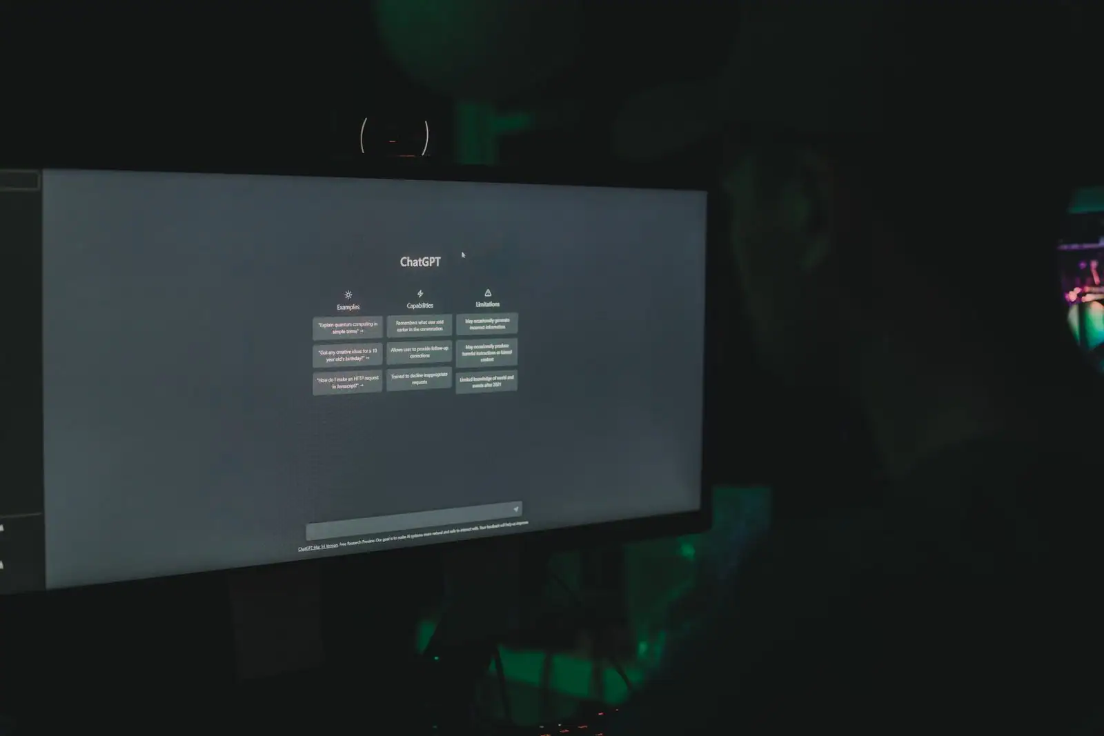Grand écran affichant la page d'accueil de ChatGPT dans une pièce sombre, silhouette en arrière-plan.