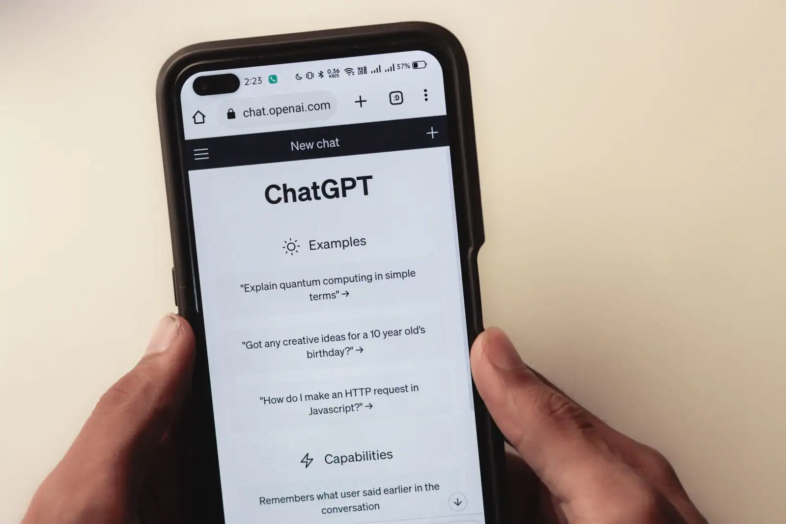 Smartphone tenu en main affichant la page d'accueil de ChatGPT à l'écran, sur fond clair.
