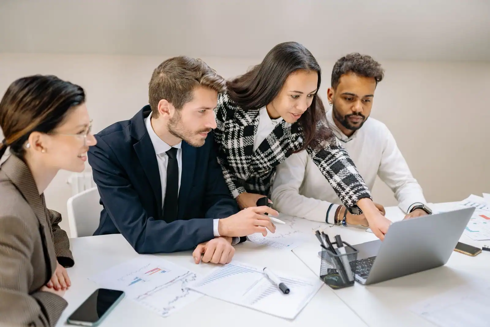 Quatre collègues réunis autour d'un ordinateur portable et de documents lors d'une réunion de travail.