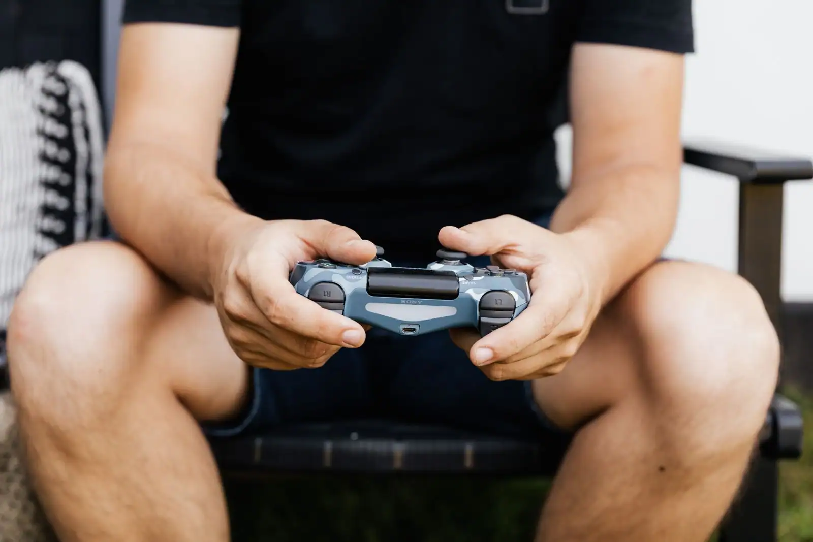 Personne assise tenant à deux mains une manette de jeu PlayStation, prête à lancer une partie