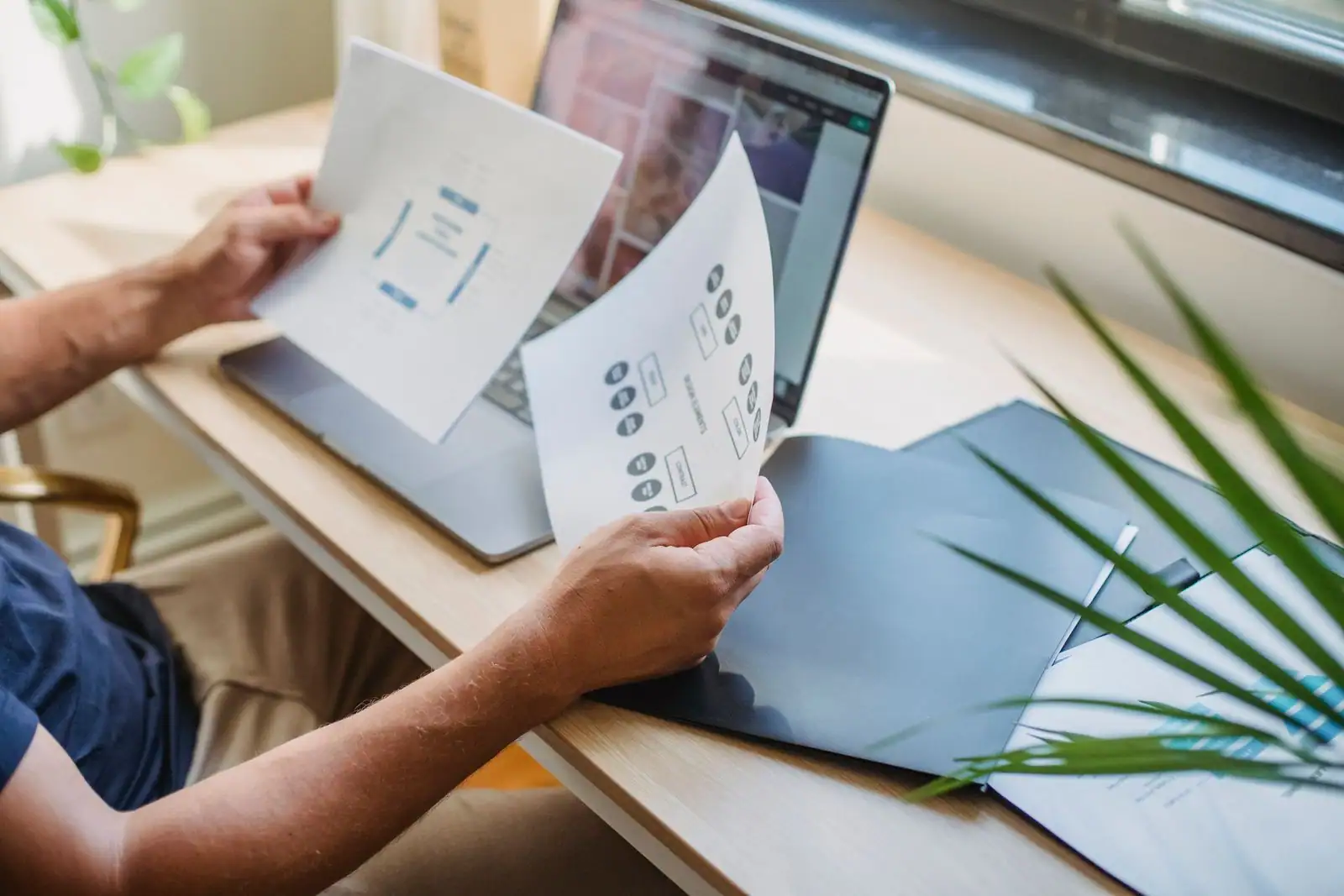 Une personne examine les maquettes papier d'un site internet, à côté de son ordinateur portable.
