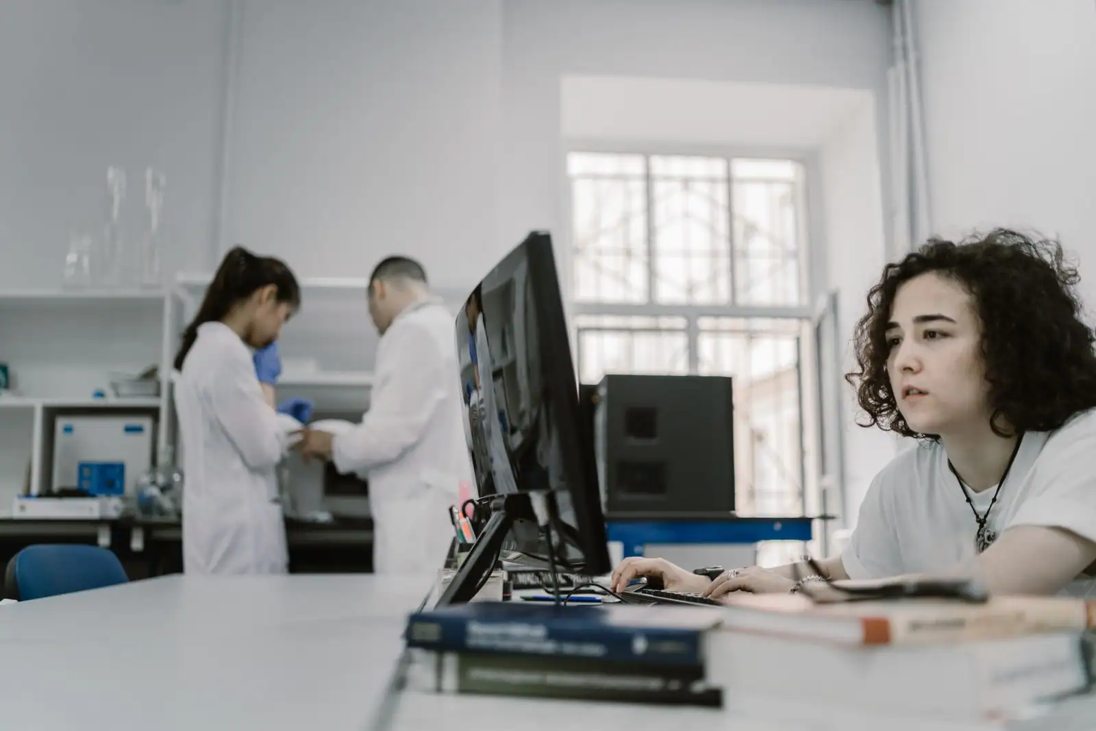 Personne concentrée sur un ordinateur dans un laboratoire, deux scientifiques en blouse blanche en arrière-plan