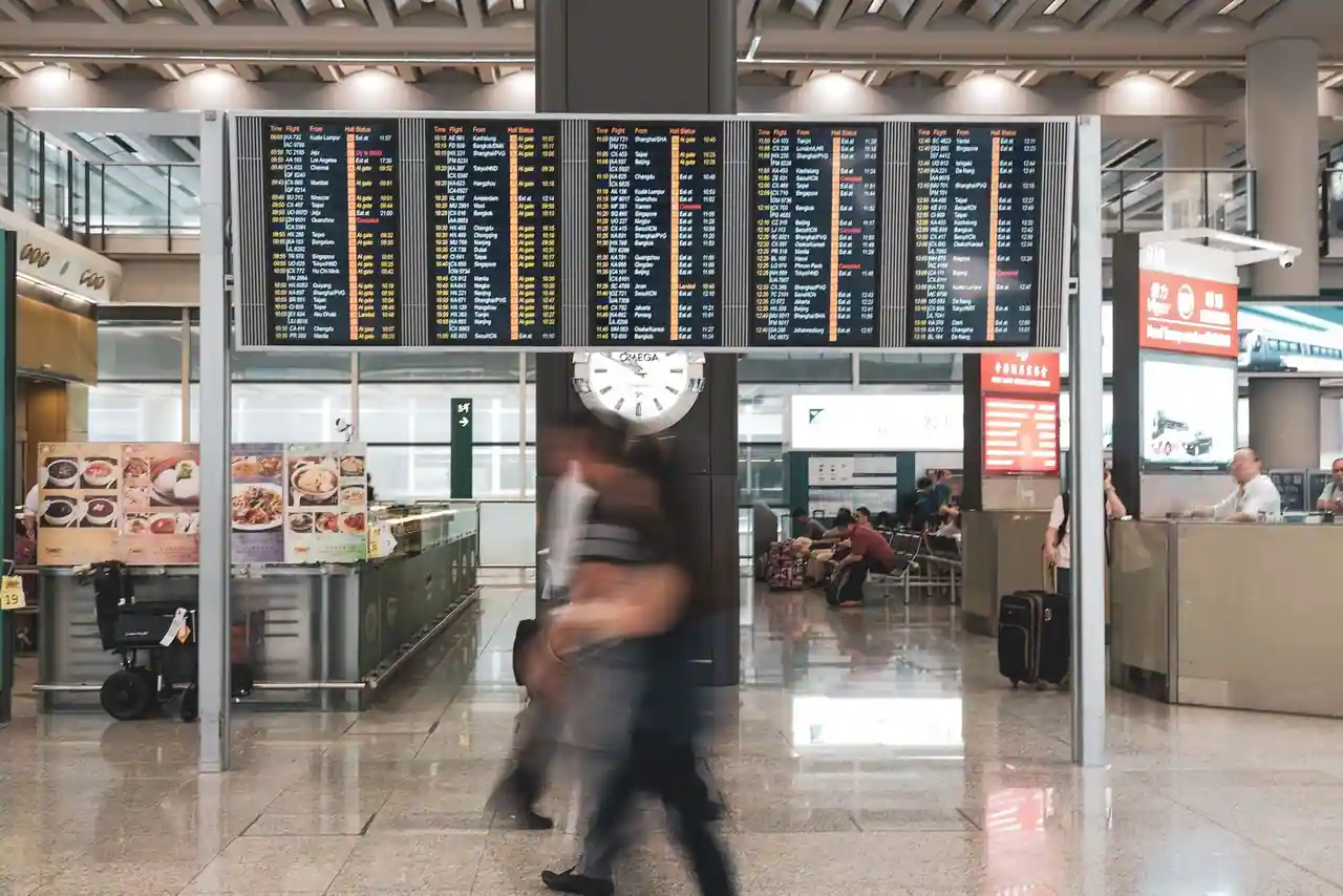 Tableau d'affichage des départs et voyageurs avec leurs bagages dans un terminal d'aéroport.