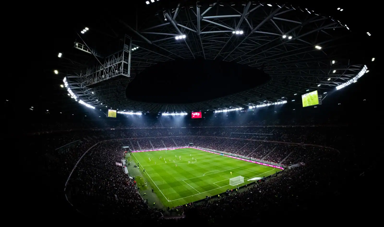 Stade de football illuminé la nuit, tribunes pleines pendant une rencontre en direct.
