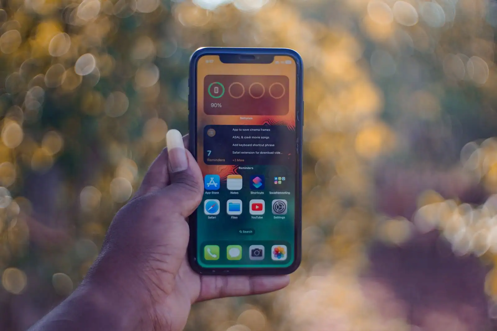 iPhone tenu en main affichant son écran d’accueil et ses applications, sur fond coloré
