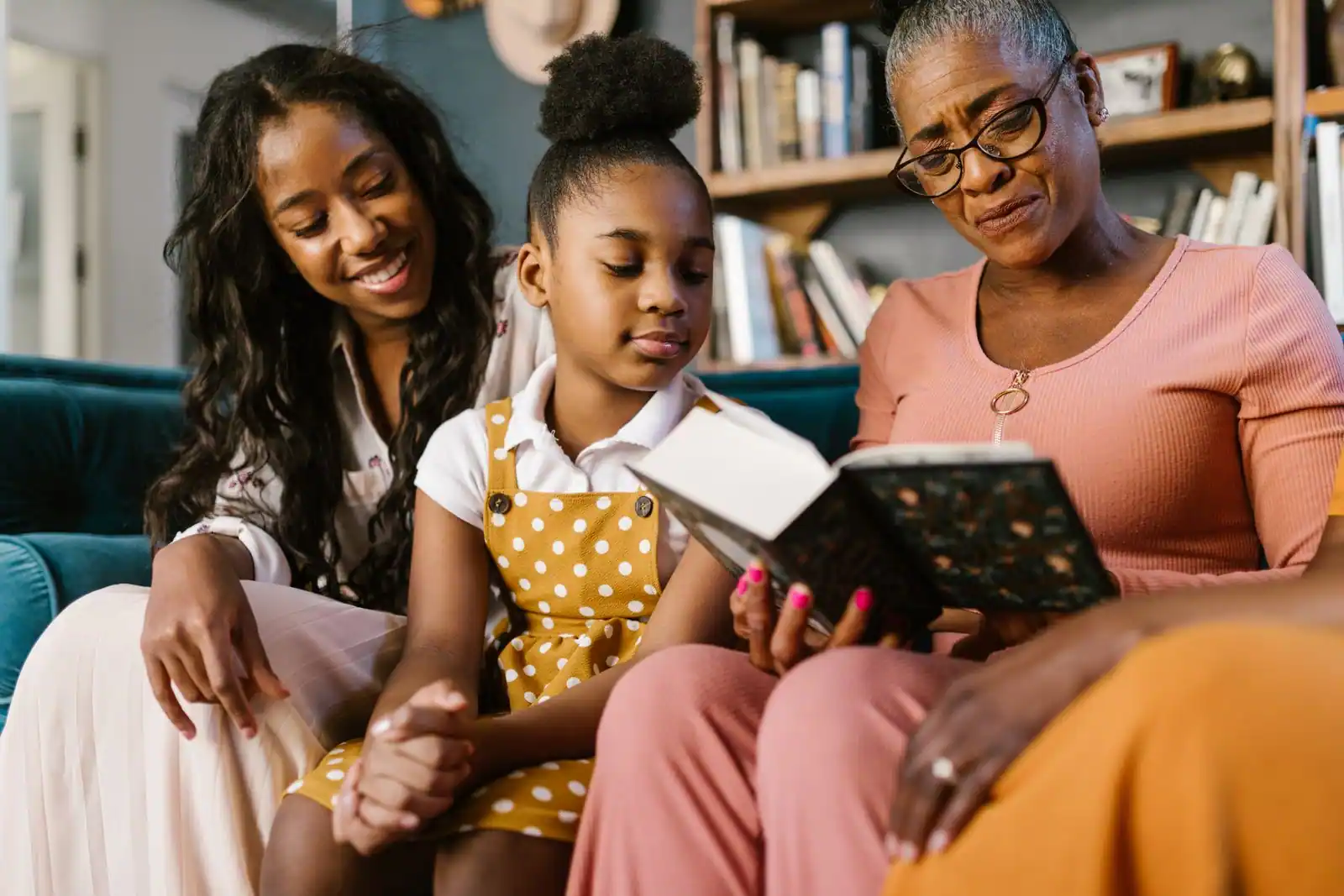 Trois générations d'une même famille lisent un livre ensemble, assises sur un canapé
