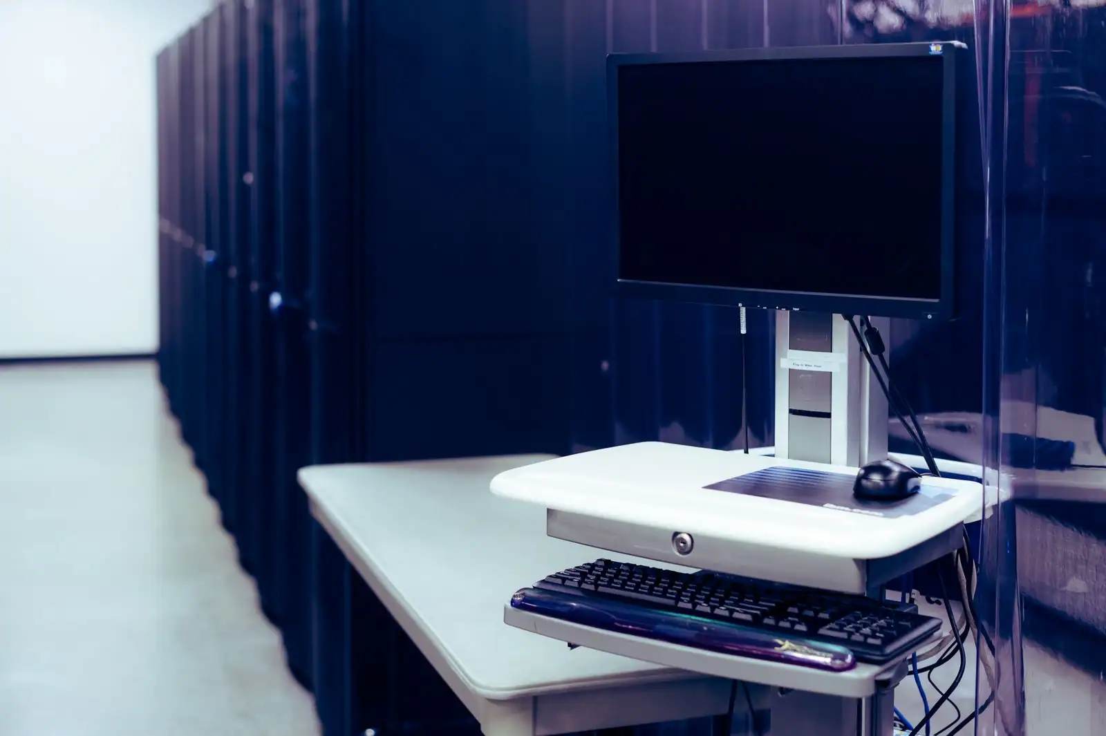 Salle de serveurs avec des baies sombres alignées et un poste de supervision écran-clavier au premier plan
