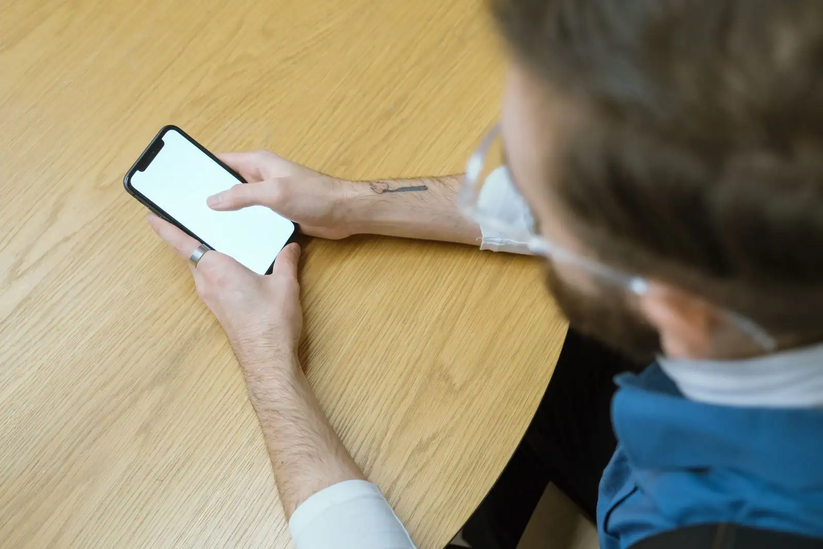 Personne tenant un smartphone à l'écran vierge, posé sur une table en bois, vue de dessus.