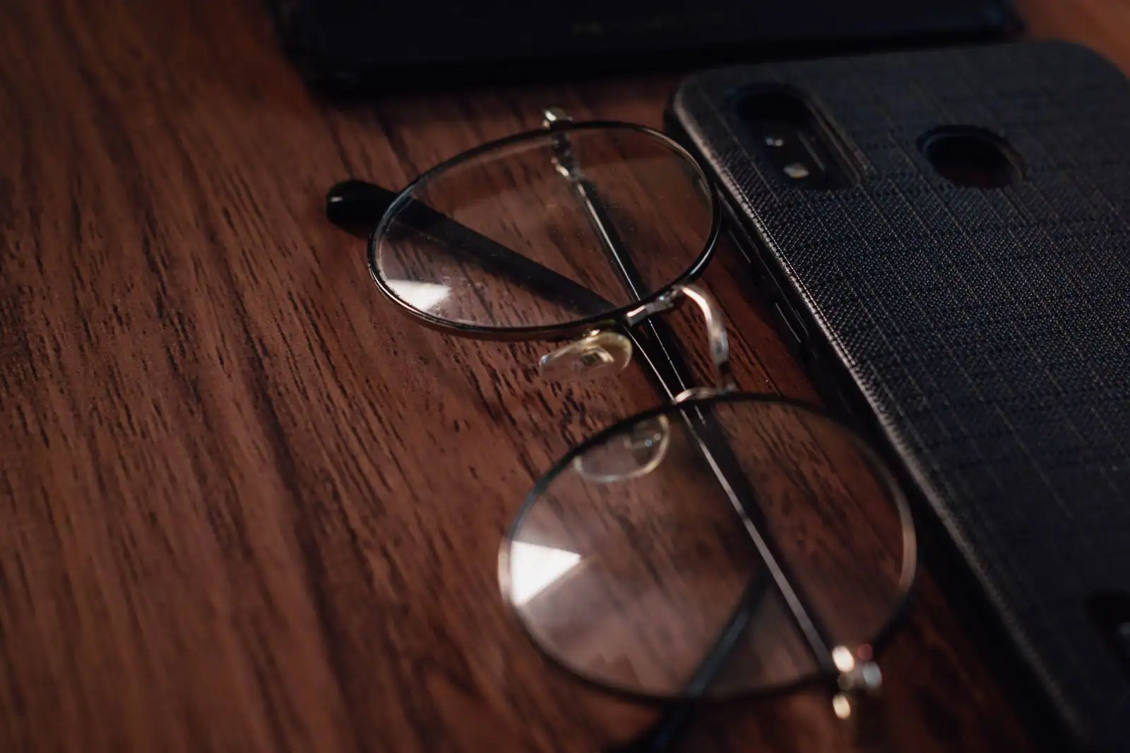 Un smartphone vu de dos, posé près d'une paire de lunettes sur une table en bois sombre