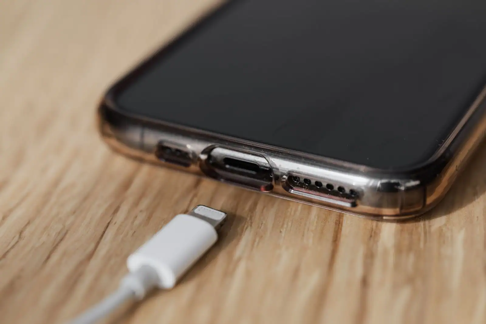 Câble de charge Lightning posé devant le port de charge d'un iPhone, sur une table en bois.