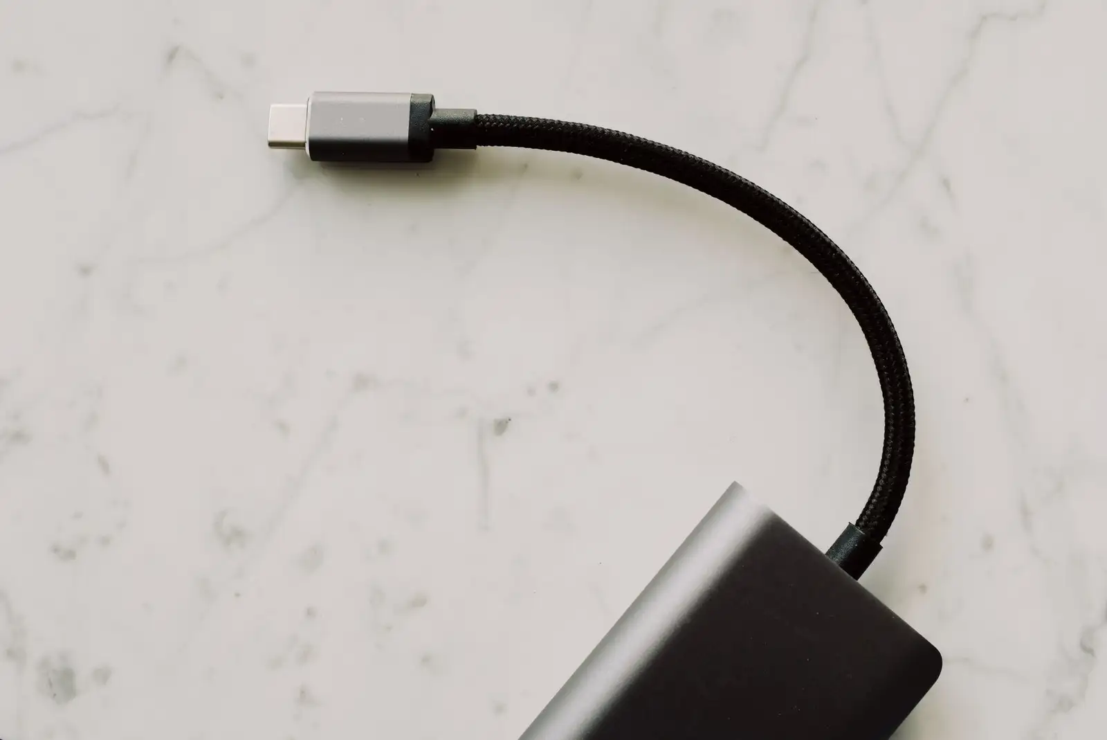 Connecteur USB-C réversible au bout d'un câble tressé, posé sur une surface en marbre clair.