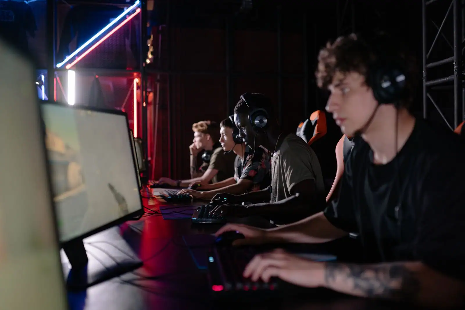 Plusieurs joueurs alignés devant des écrans d'ordinateur, casque audio et mains sur le clavier de jeu