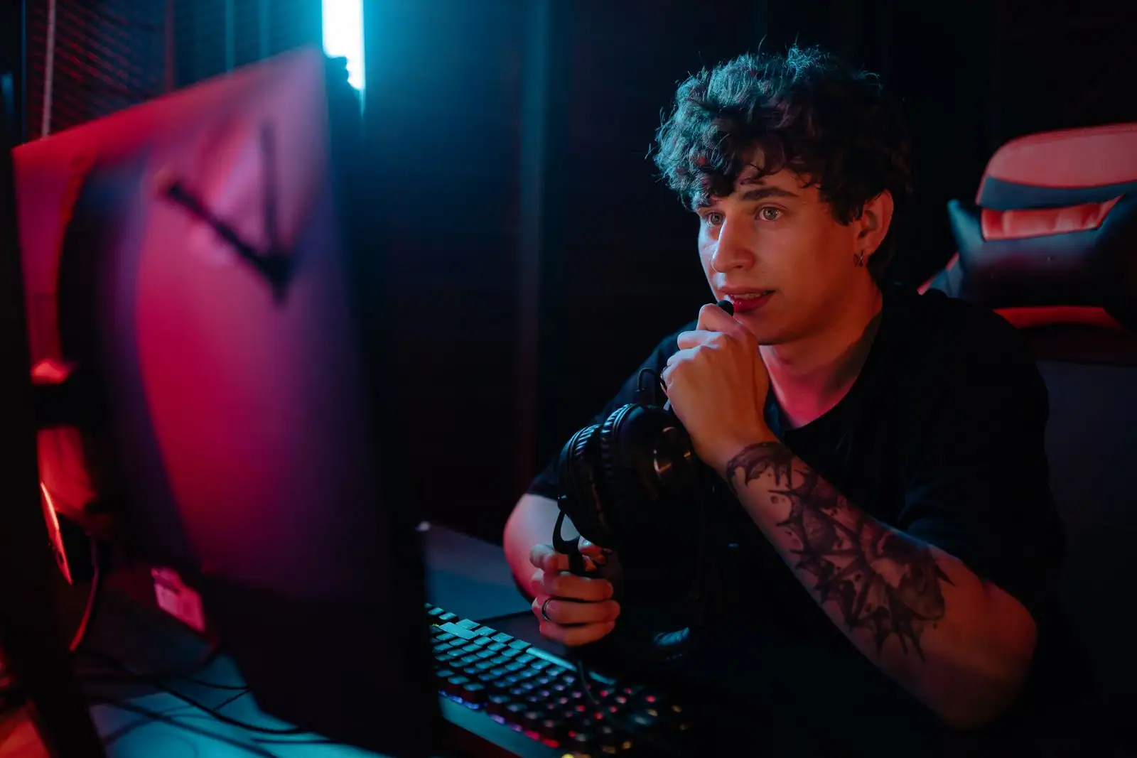 Jeune joueur devant l'écran de son ordinateur dans un setup PC à l'éclairage néon, casque à la main