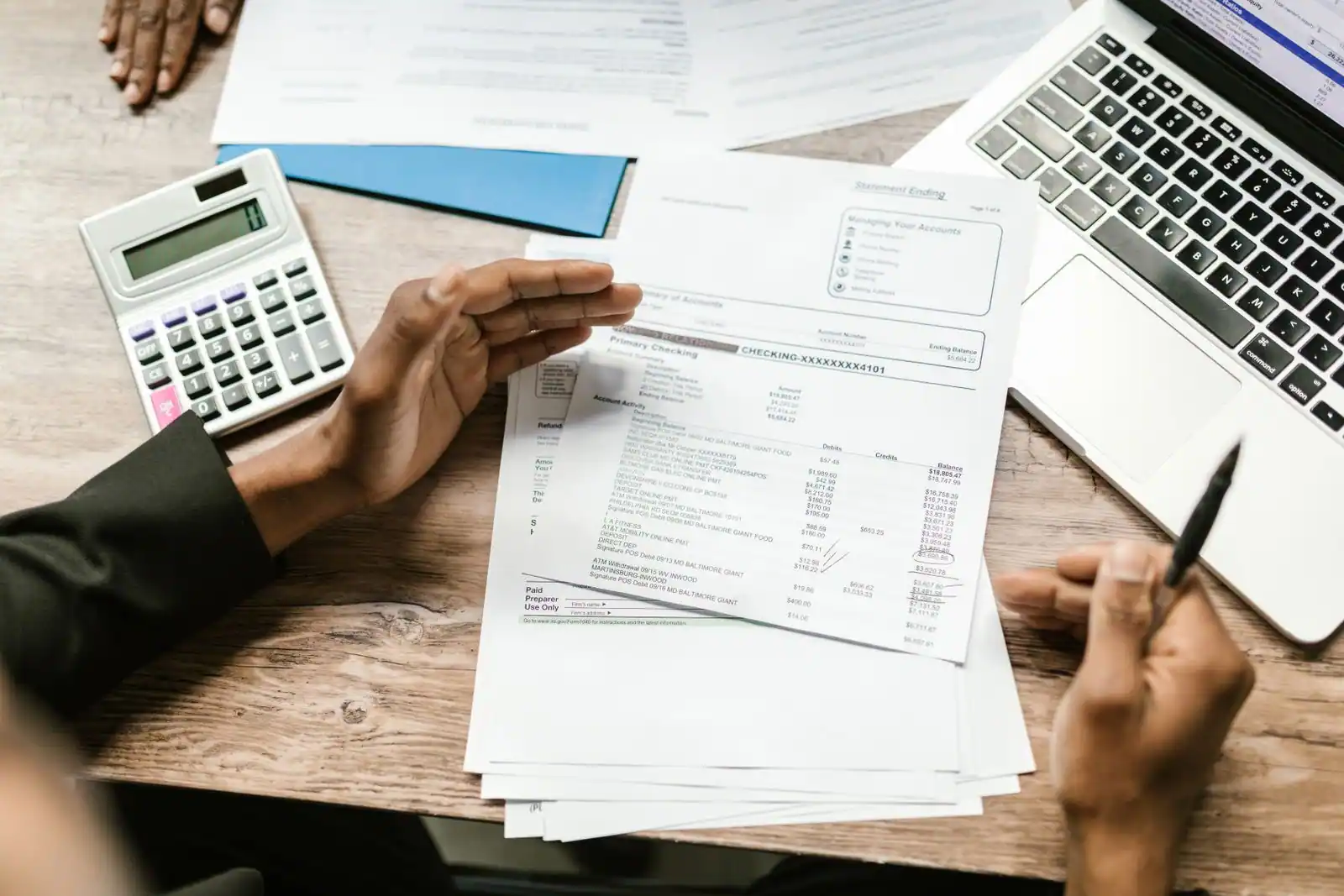 Mains examinant des relevés comptables avec une calculatrice et un ordinateur portable sur un bureau.