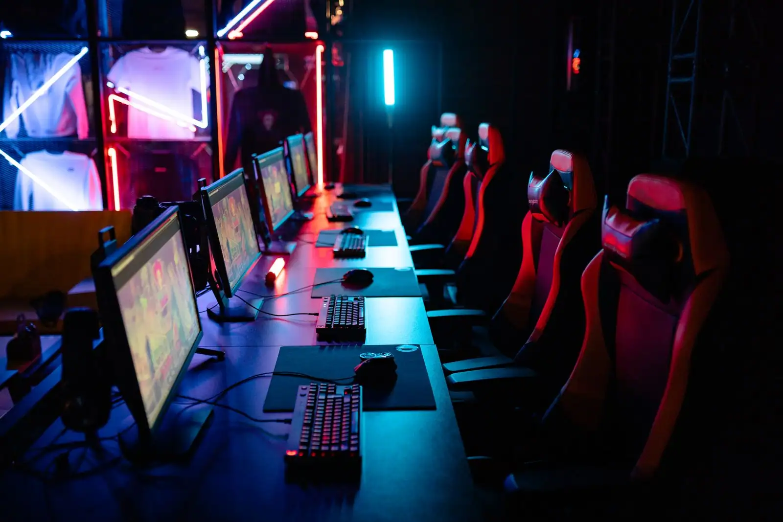 Salle d'esport avec une rangée d'ordinateurs de jeu, écrans allumés, fauteuils gaming et néons colorés.