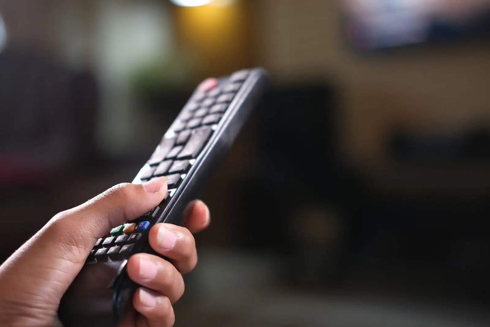 Main tenant une télécommande de télévision pointée vers un téléviseur dans un salon