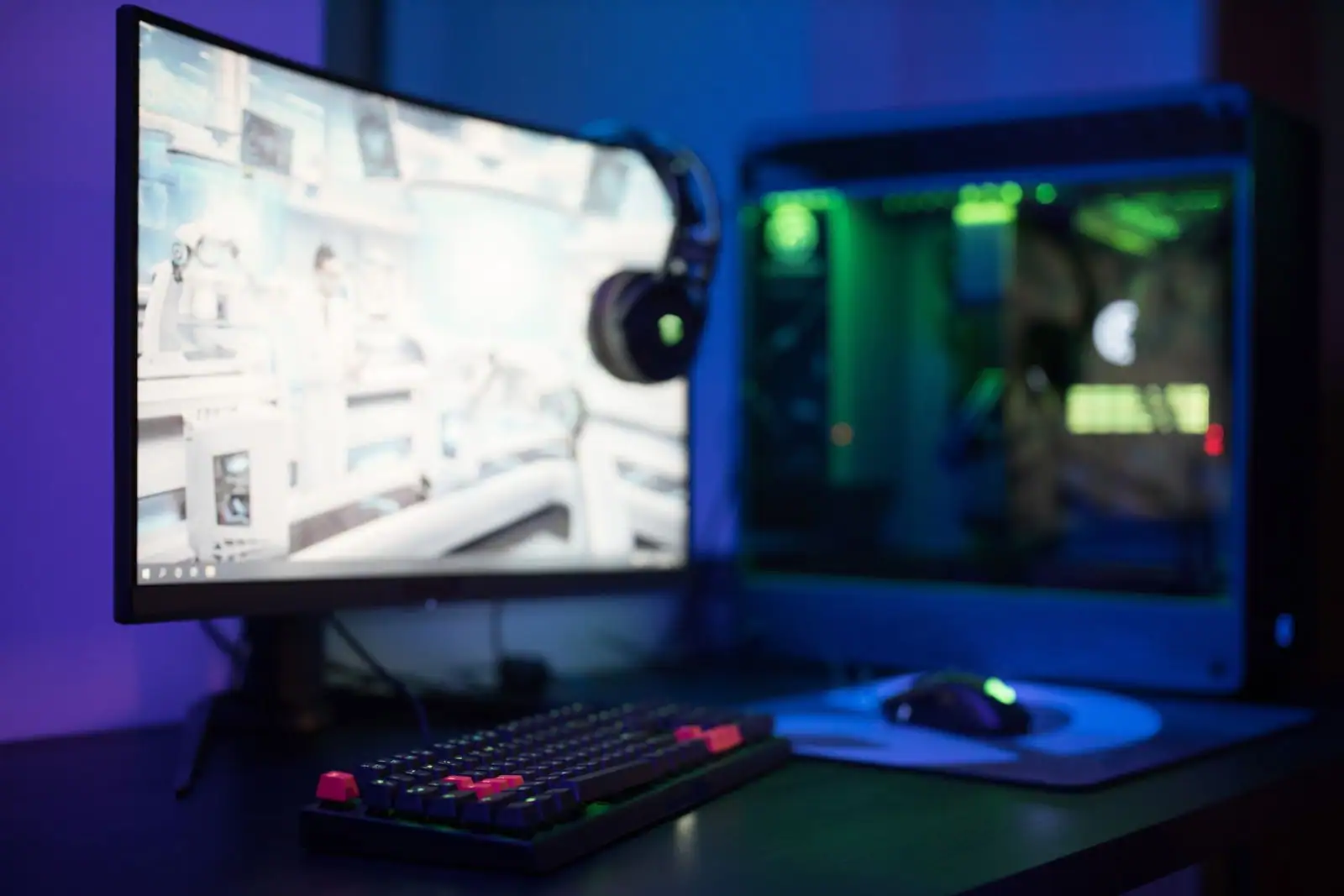 Poste de jeu sur PC avec écran allumé, clavier de gaming, souris et casque dans une lumière bleutée.