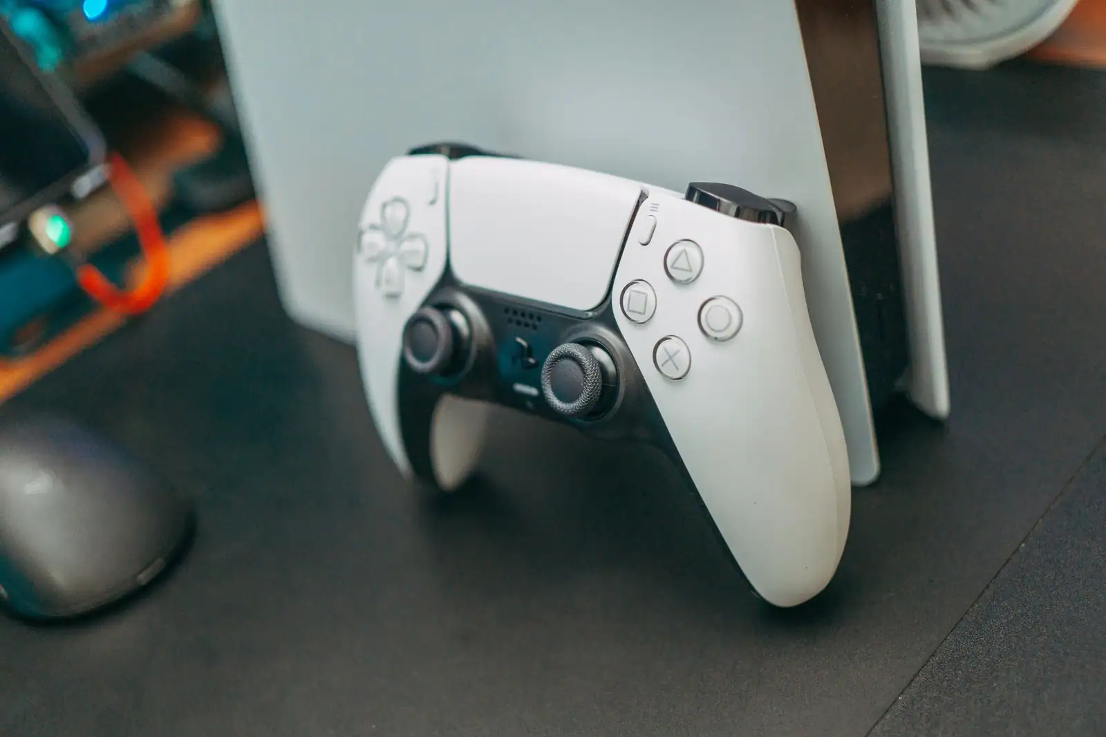 Manette DualSense blanche de PlayStation 5 posée contre la console PS5, sur un bureau sombre.