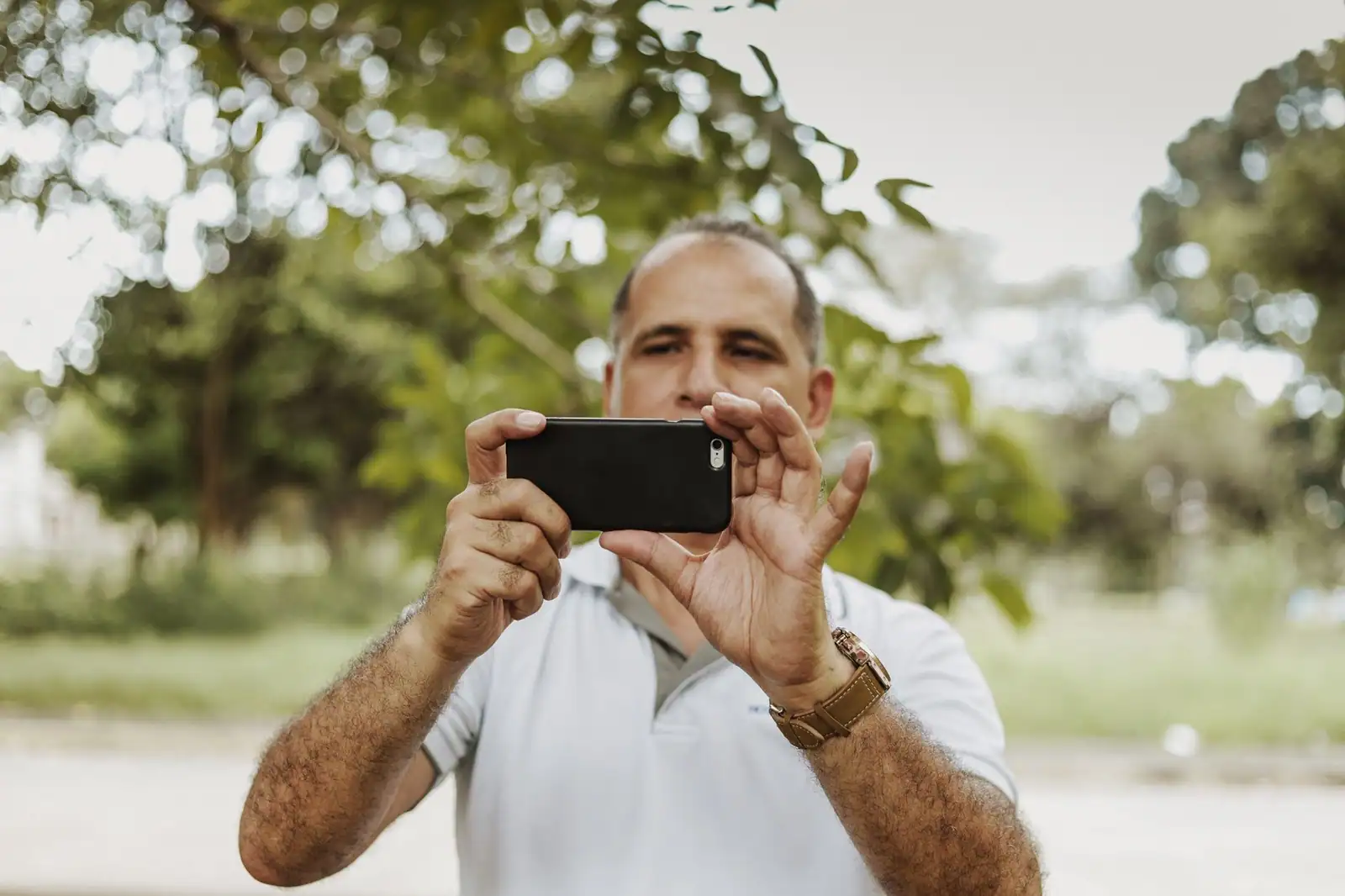 Homme photographiant une scène en extérieur avec son smartphone tenu à l'horizontale à deux mains