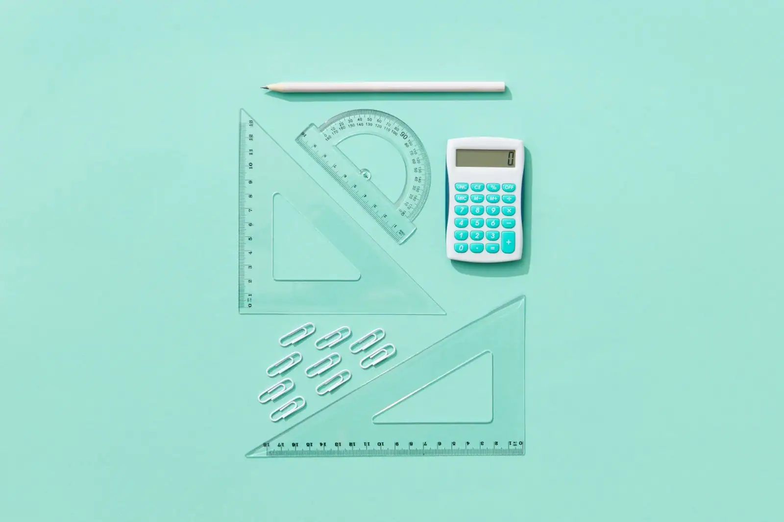 Calculatrice, règles, équerres et rapporteur disposés à plat sur un fond turquoise.