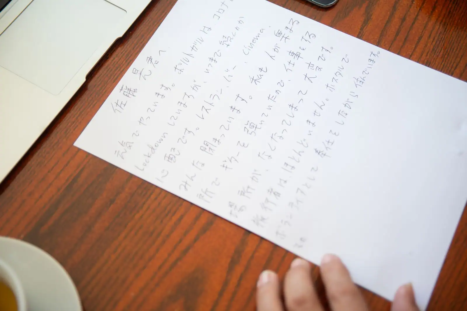 Feuille de papier couverte de texte japonais manuscrit, tenue à la main sur un bureau en bois.