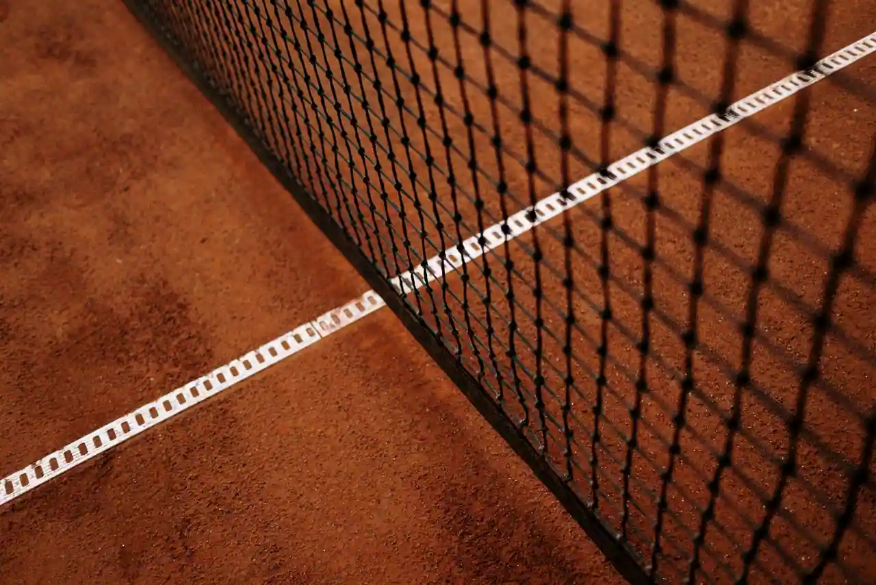 Gros plan sur le filet et la ligne blanche d'un court de tennis en terre battue ocre.