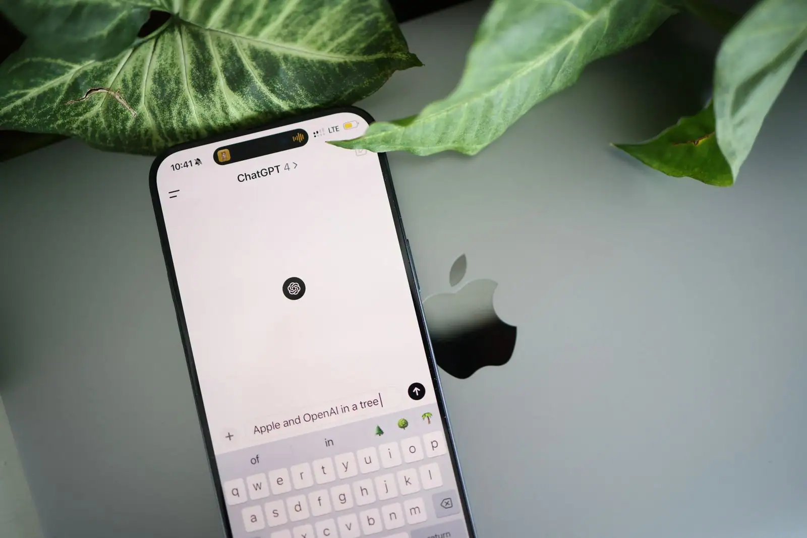 Smartphone affichant l'application ChatGPT, posé sur un ordinateur portable au milieu de feuilles vertes.