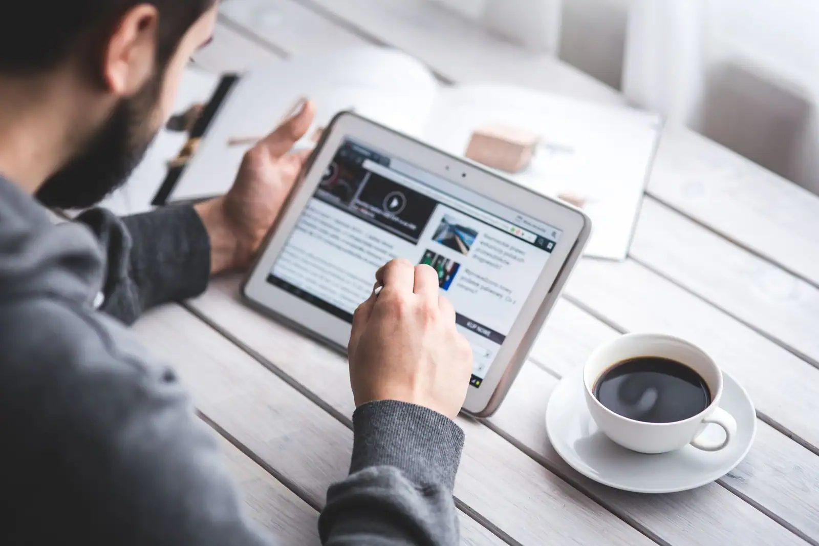 Homme lisant un site d'actualité sur une tablette posée sur une table en bois, une tasse de café à côté
