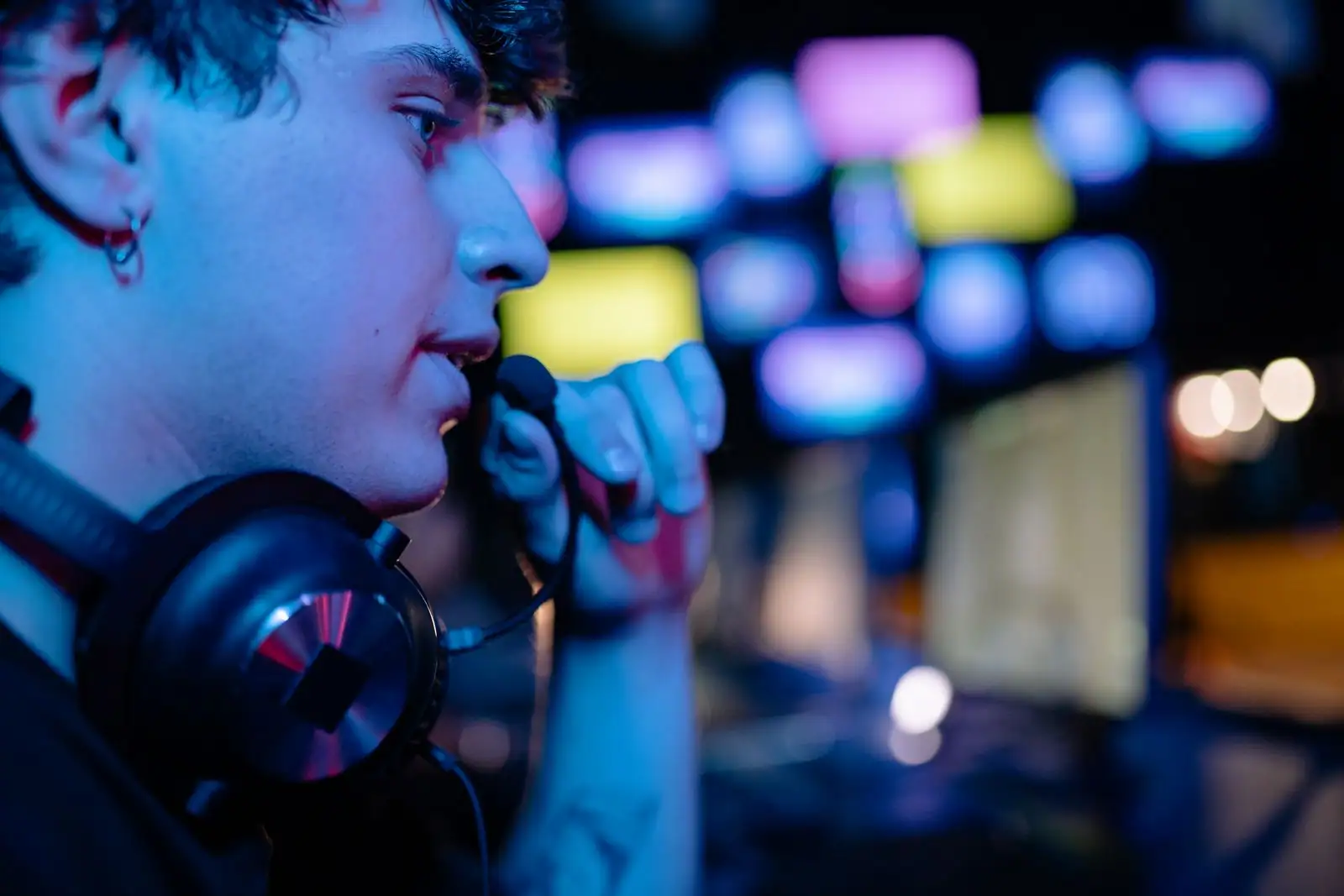 Jeune streamer au casque audio autour du cou, micro à la main, devant des écrans aux lumières bleutées