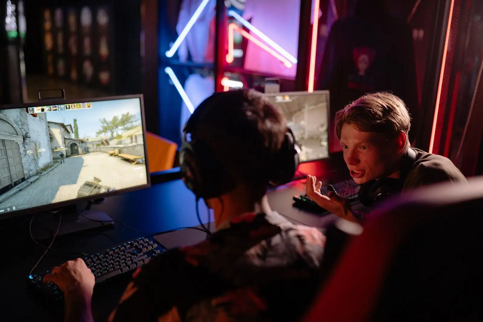 Deux jeunes joueurs devant leurs écrans dans une installation gaming aux néons colorés.