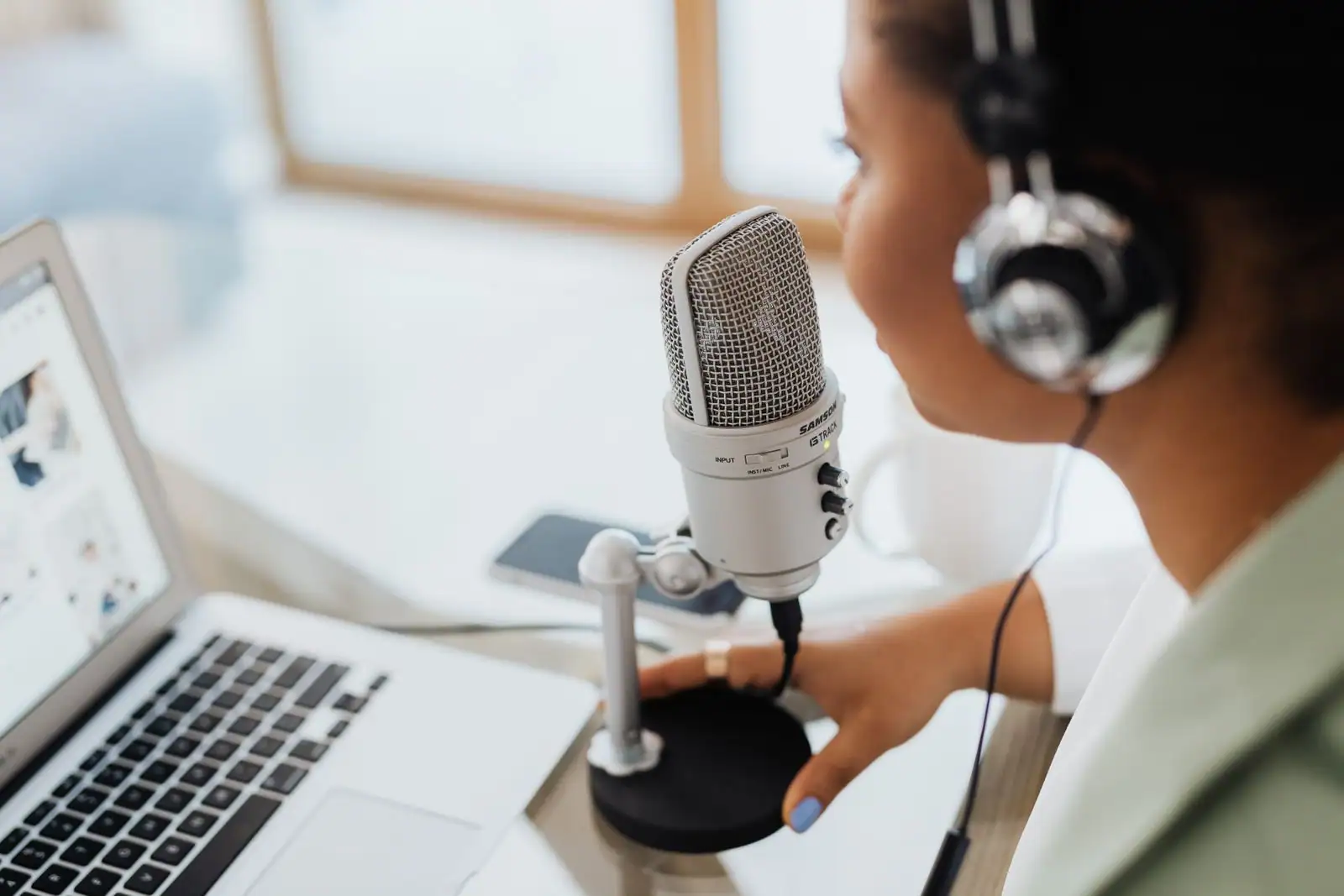 Femme portant un casque audio, parlant dans un grand micro à condensateur, un ordinateur portable ouvert à côté.