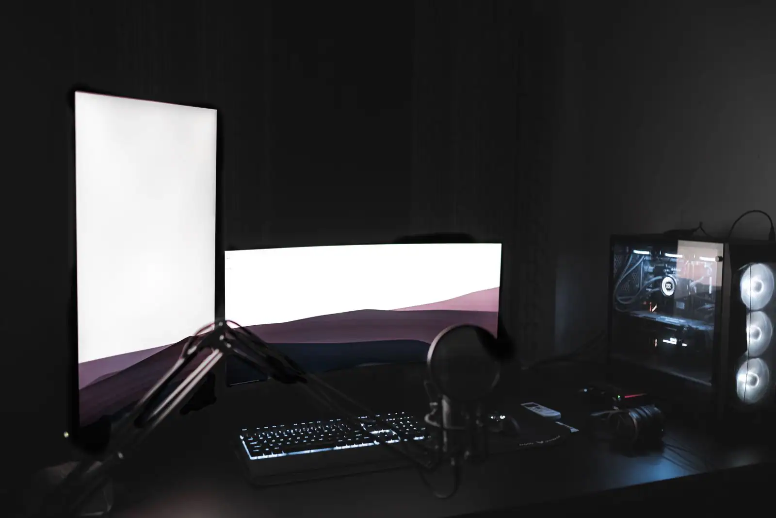 Poste de streaming dans une pièce sombre : deux écrans allumés, clavier rétroéclairé, micro à condensateur et tour PC RGB