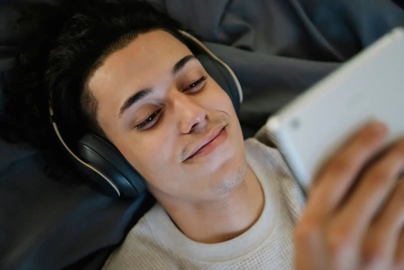 Une personne allongée regarde une vidéo sur une tablette, un casque audio sur les oreilles.