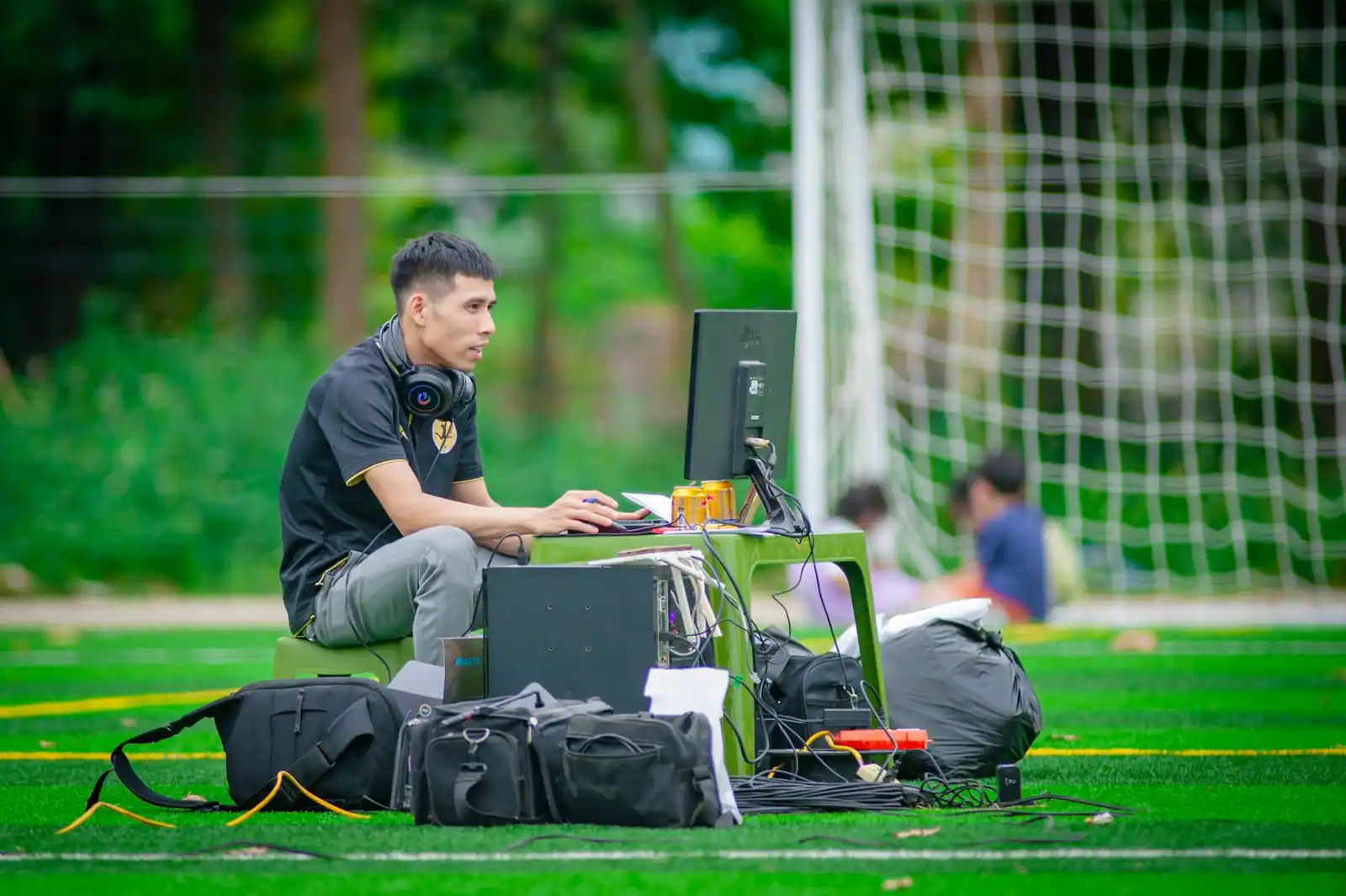 Homme installé à un ordinateur sur un terrain de football, casque audio autour du cou