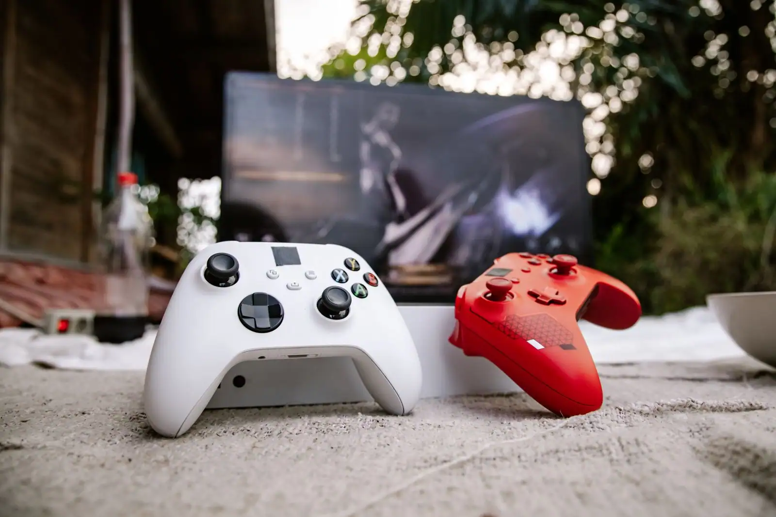 Deux manettes Xbox sans fil, une blanche et une rouge, devant un écran affichant un jeu vidéo.