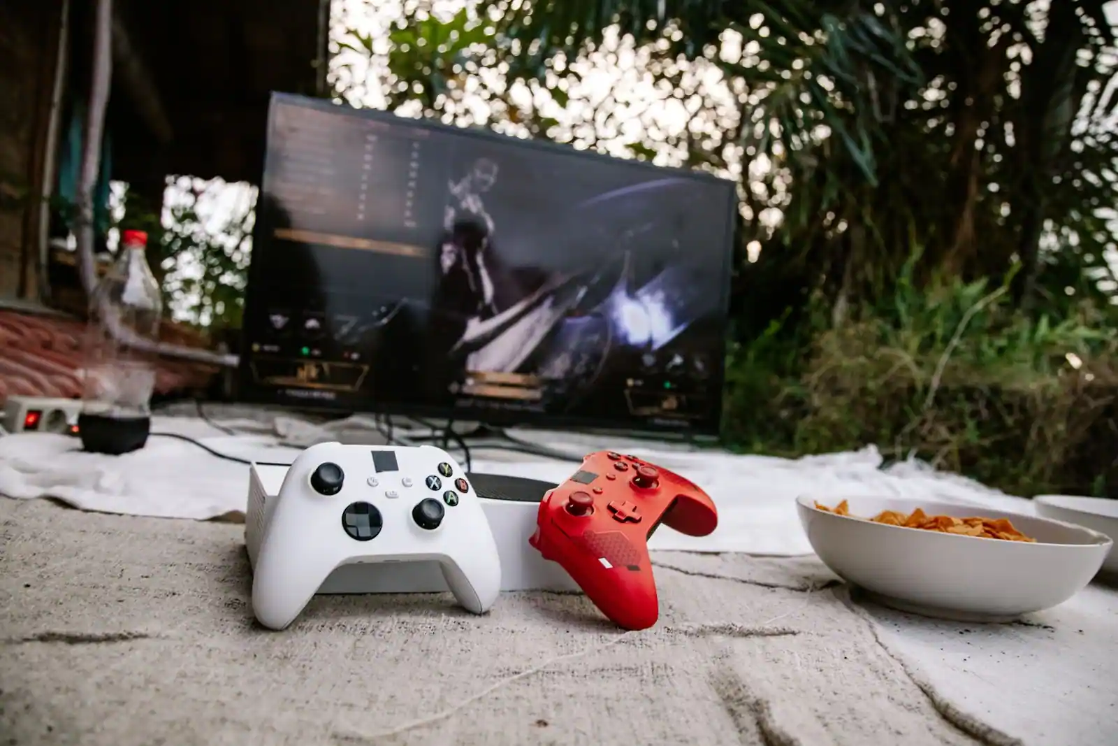 Deux manettes Xbox, une blanche et une rouge, posées devant un écran affichant un jeu vidéo.