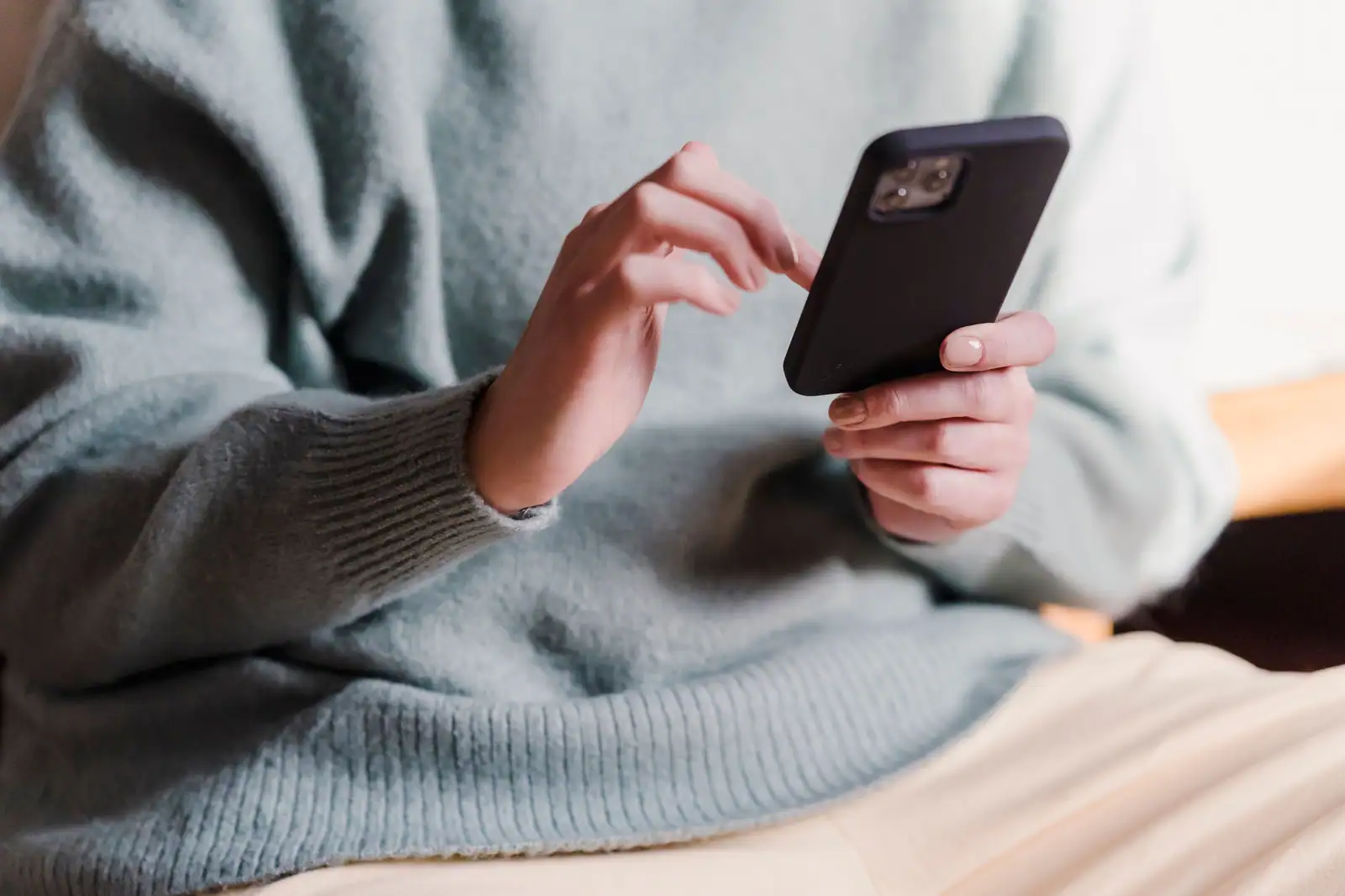 Personne tenant un téléphone à la verticale, le doigt prêt à faire défiler l'écran, dans un intérieur clair