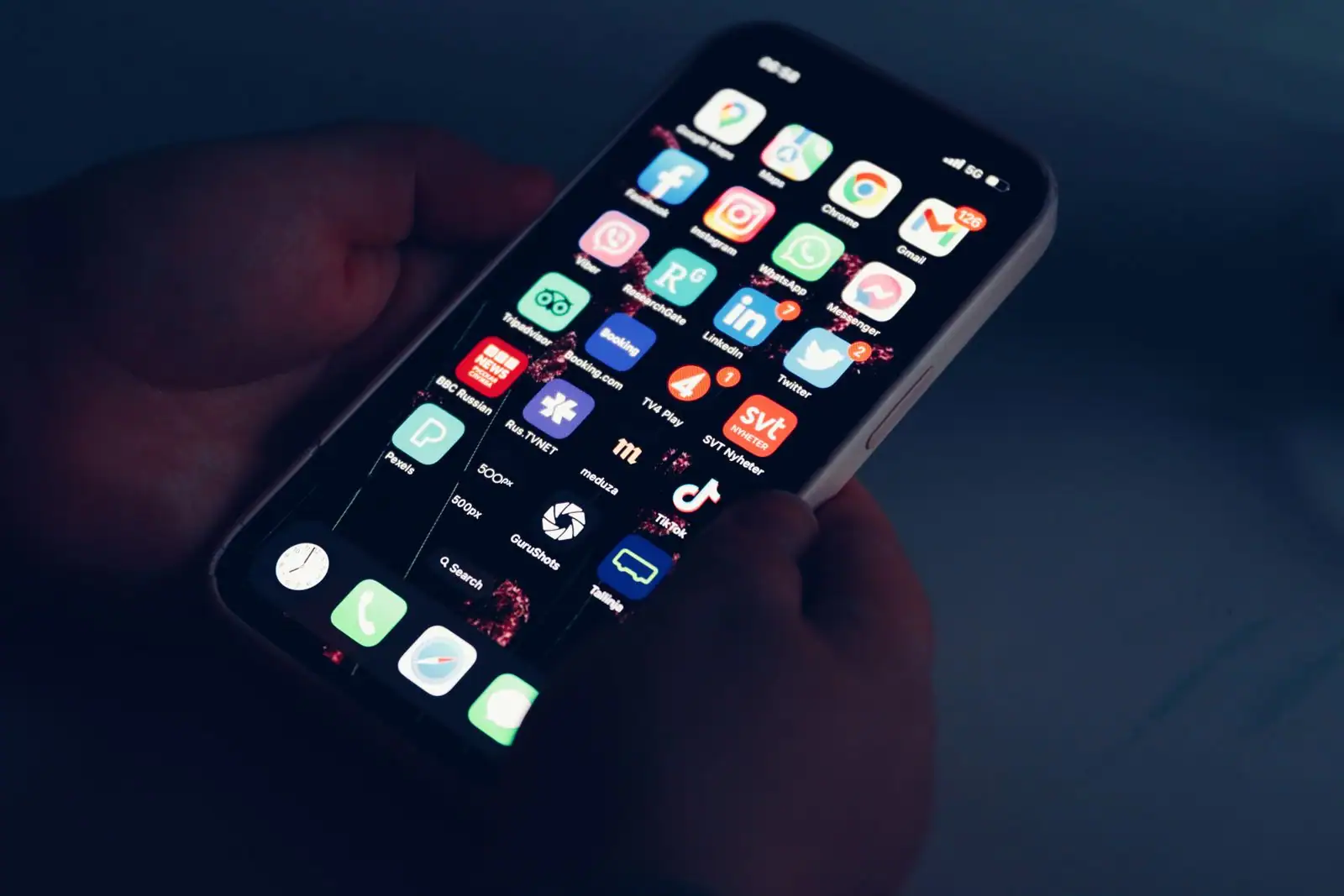 Main tenant un smartphone dont l’écran d’accueil affiche une grille dense d’icônes d’applications.