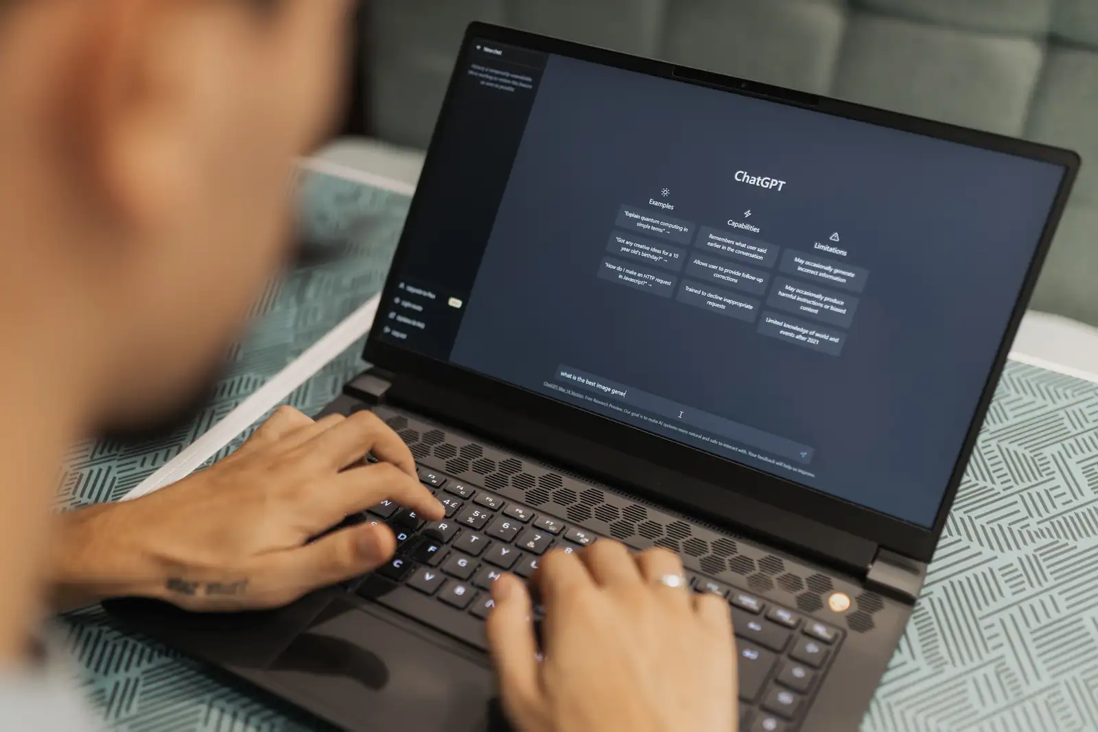 Mains sur le clavier d'un ordinateur portable affichant l'interface de ChatGPT et ses exemples de requêtes