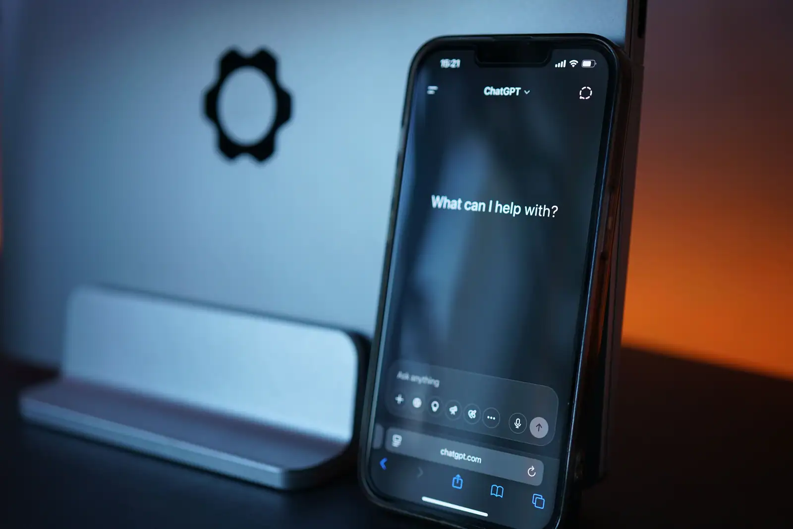 Smartphone affichant l'écran d'accueil de ChatGPT, posé contre le pied d'un écran d'ordinateur.