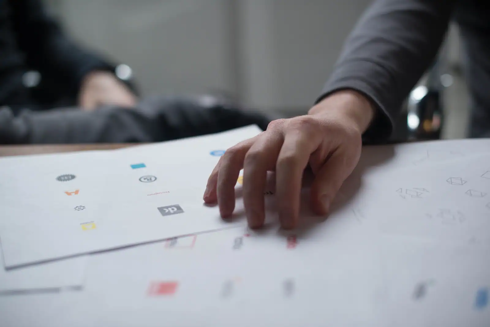 Main posée sur des planches imprimées présentant une série de petits logos en couleur.