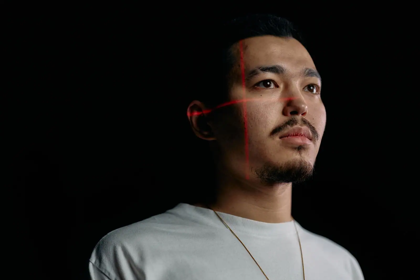 Lignes laser rouges croisant le visage d'un homme sur fond noir, évoquant une analyse faciale automatisée.