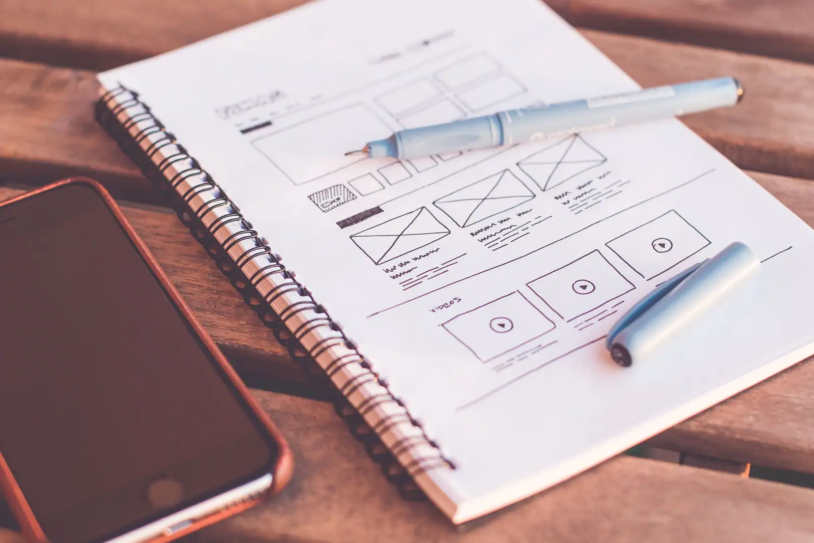 Carnet à spirale ouvert sur un croquis de page web tracé au feutre, avec un smartphone posé à côté.