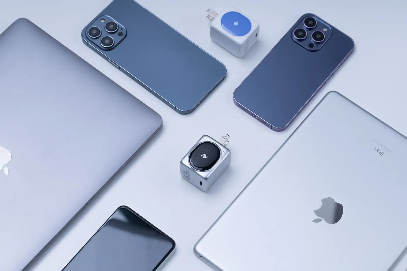 Un MacBook, deux iPhone et un iPad posés côte à côte sur un fond clair, vus de dessus.