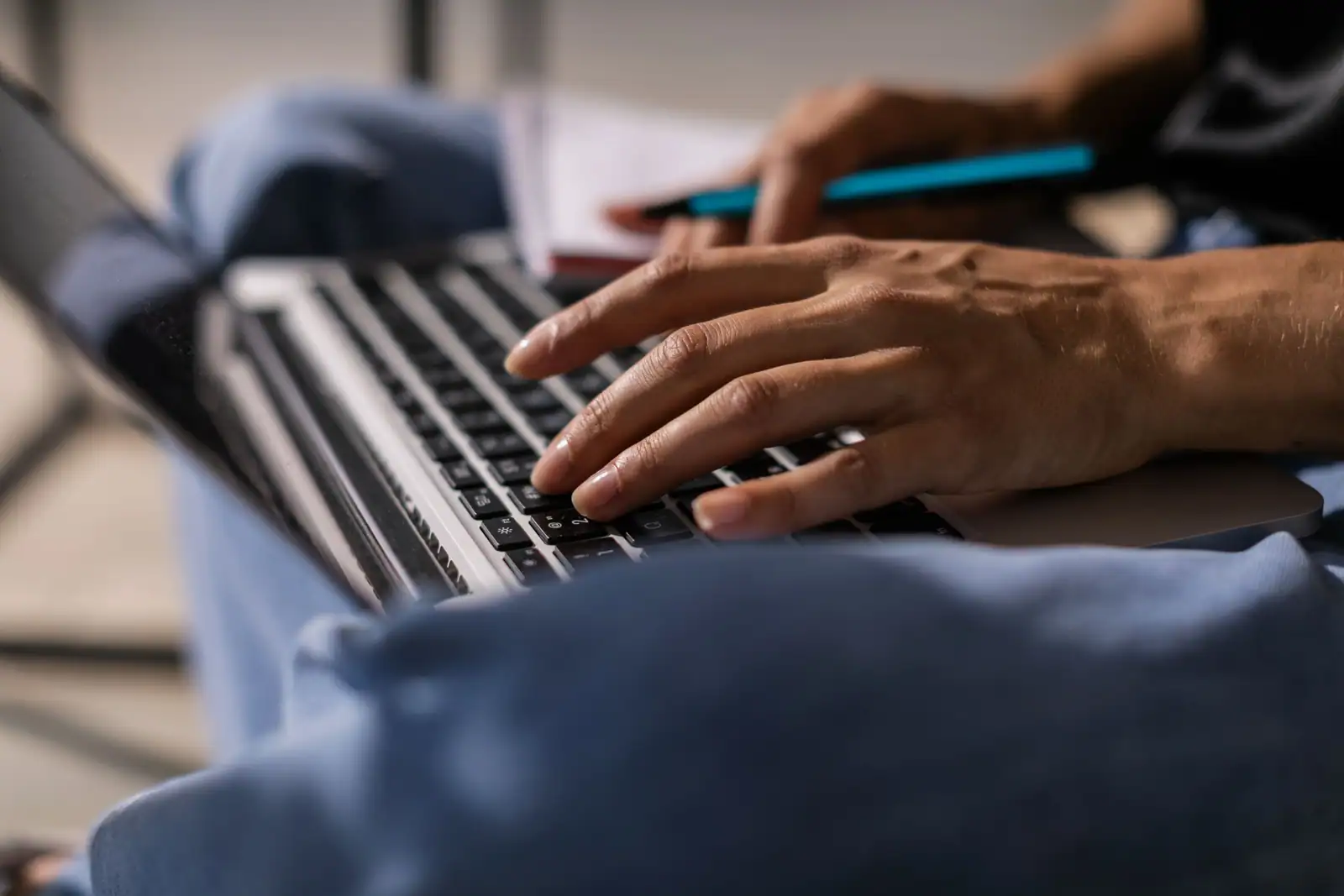 Mains posées sur le clavier d’un ordinateur portable, un carnet et un stylo posés juste à côté.