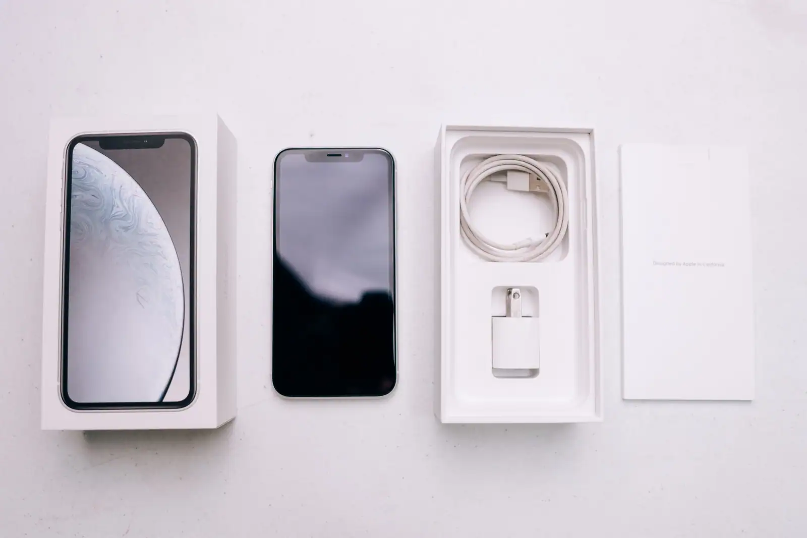 iPhone posé à côté de sa boîte ouverte, avec le câble, l'adaptateur et la notice, vus de dessus.